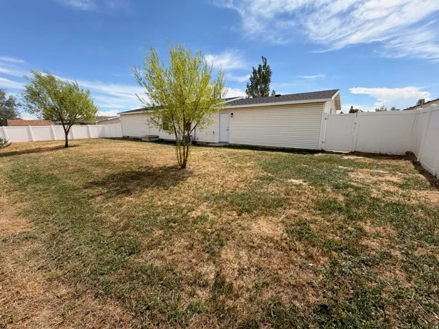 Spacious backyard featuring a level lawn with mature shade trees and white vinyl fencing, offering ample outdoor space and privacy