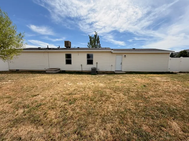 Rear exterior featuring tan siding, multiple windows, a white entry door, and a partially fenced yard