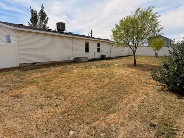 Expansive backyard featuring a vinyl privacy fence, mature trees, and a low-maintenance siding exterior