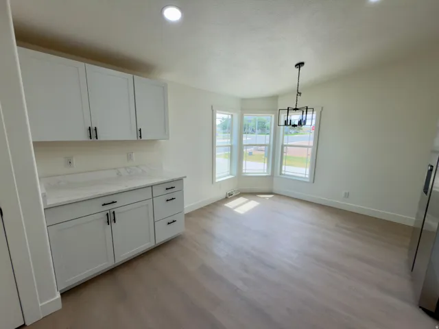 White shaker cabinetry with matte black hardware, stone-finish countertops, wood-finish flooring, a bay window, and a contemporary chandelier