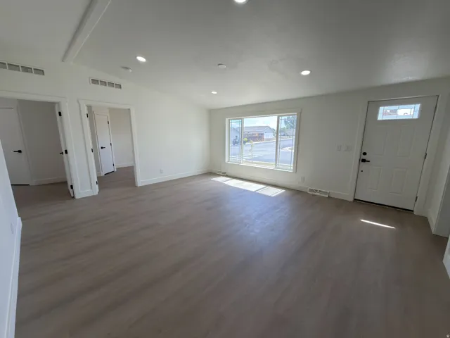 Open-concept living area featuring wood-finish flooring, recessed lighting, and a white paneled entry door with transom glass