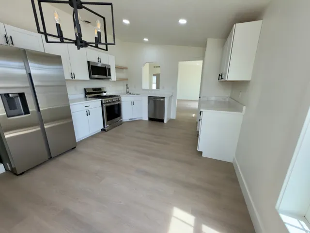 Kitchen featuring stainless steel appliances, white cabinetry, wood-finish flooring, recessed lighting, and a modern chandelier