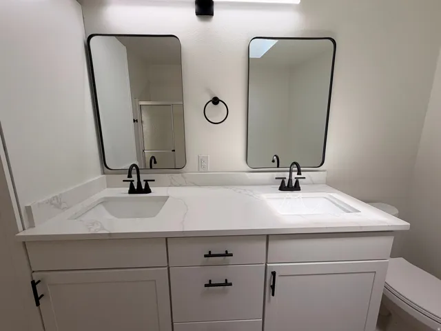 Dual vanity with white cabinetry, integrated sinks, white countertops, and black fixtures
