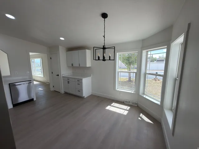 Expansive wood-finish flooring, crisp white cabinetry, stainless steel dishwasher, modern chandelier, and a bay window