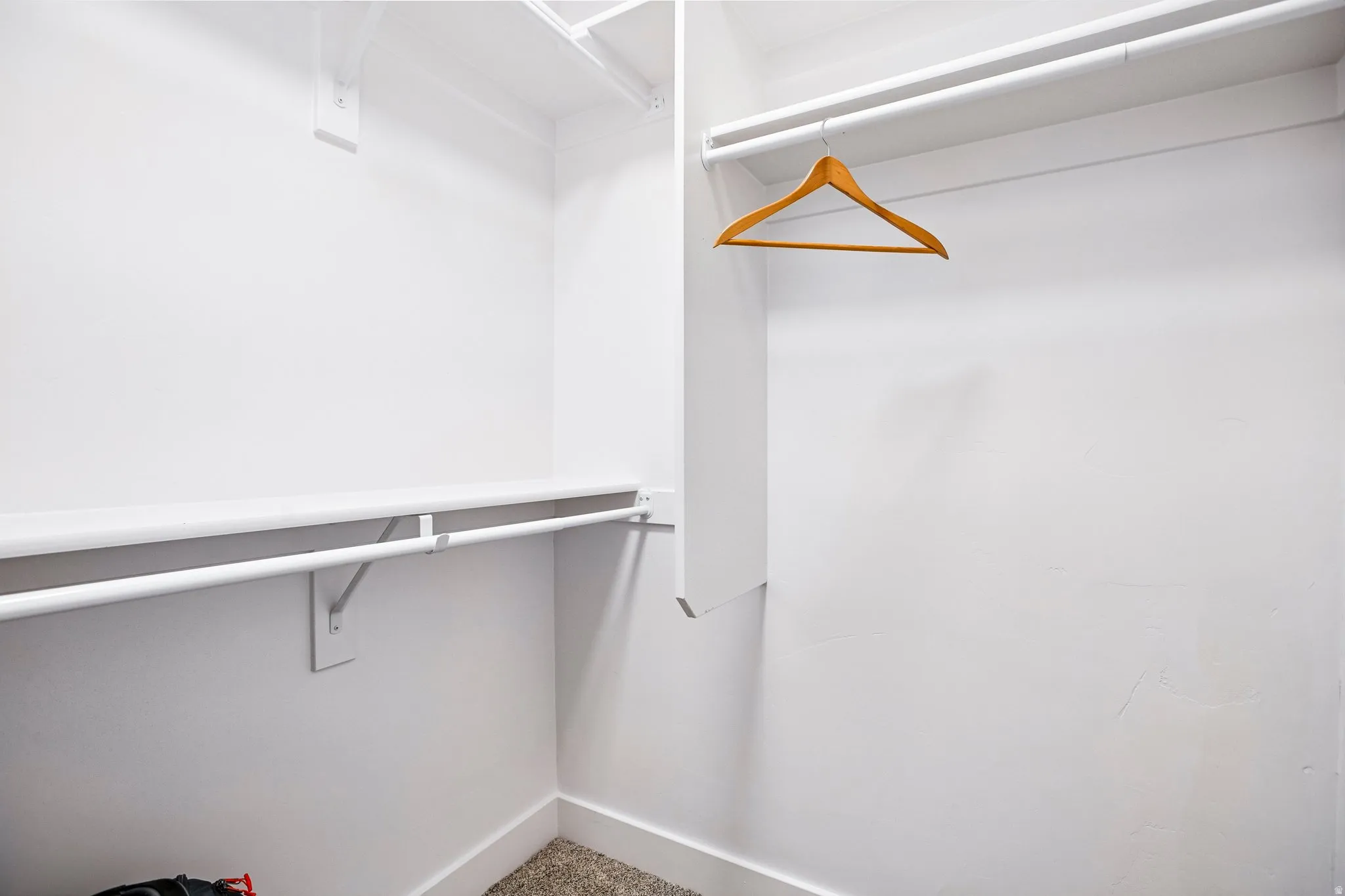 Spacious walk-in closet featuring white painted walls, polished concrete flooring, a sturdy metal hanging rod, and wooden hanger—ideal for organized storage and wardrobe display