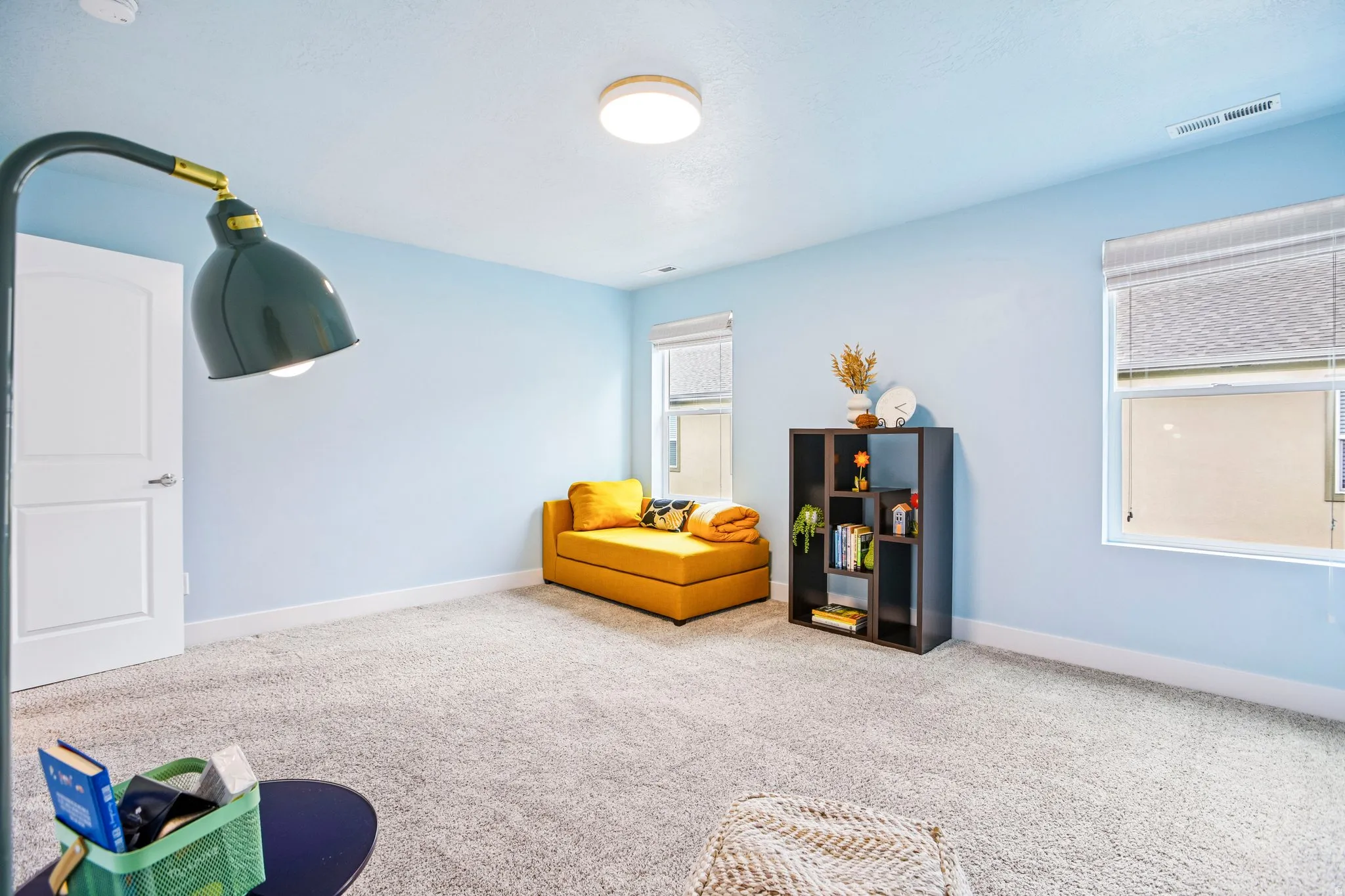 Recessed ceiling light, two windows with blinds, light blue walls, and light-colored carpet flooring