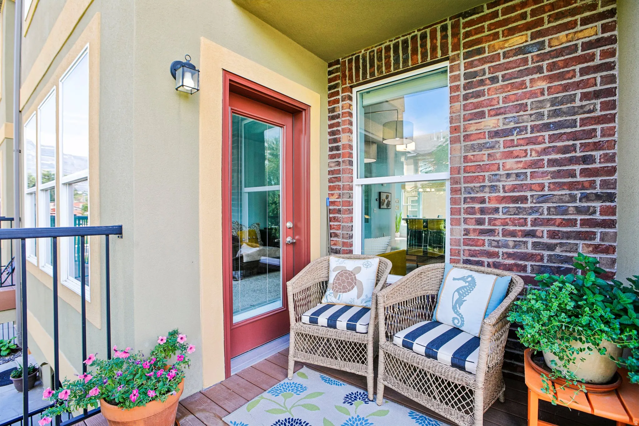 Exterior balcony featuring a wood-finish deck, brick accent wall, and a full-light entry door