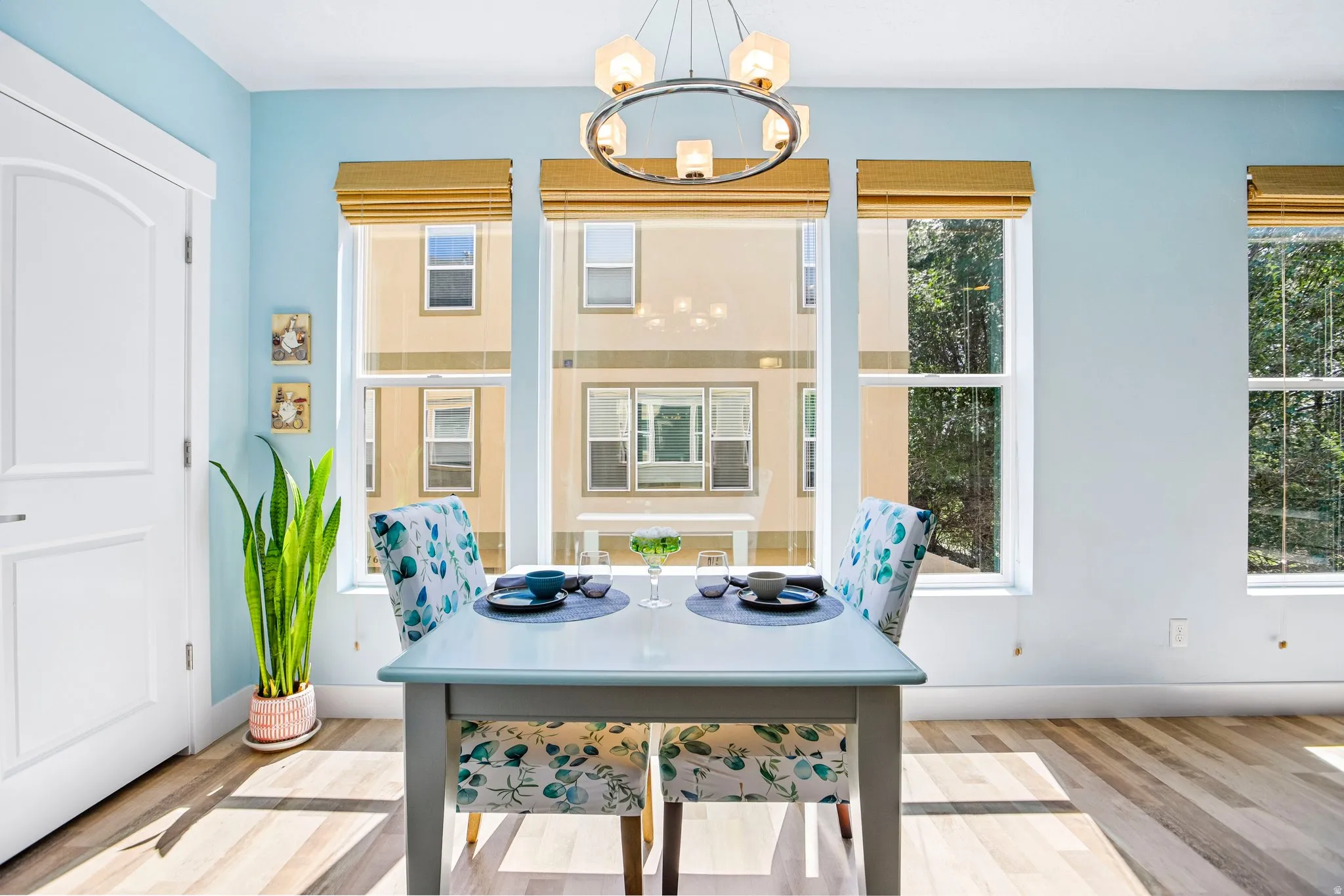 Bright dining area flooded with natural light through multiple multi-pane windows with gold-toned Roman shades
