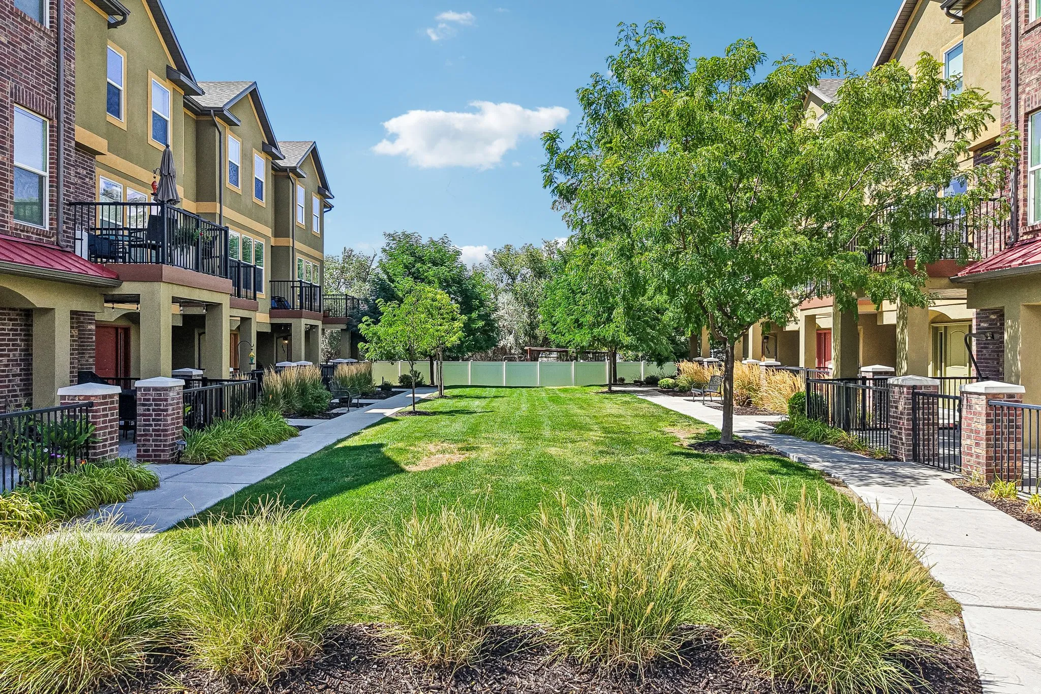 Manicured lawn with mature shade trees and ornamental grasses creates an inviting courtyard setting
