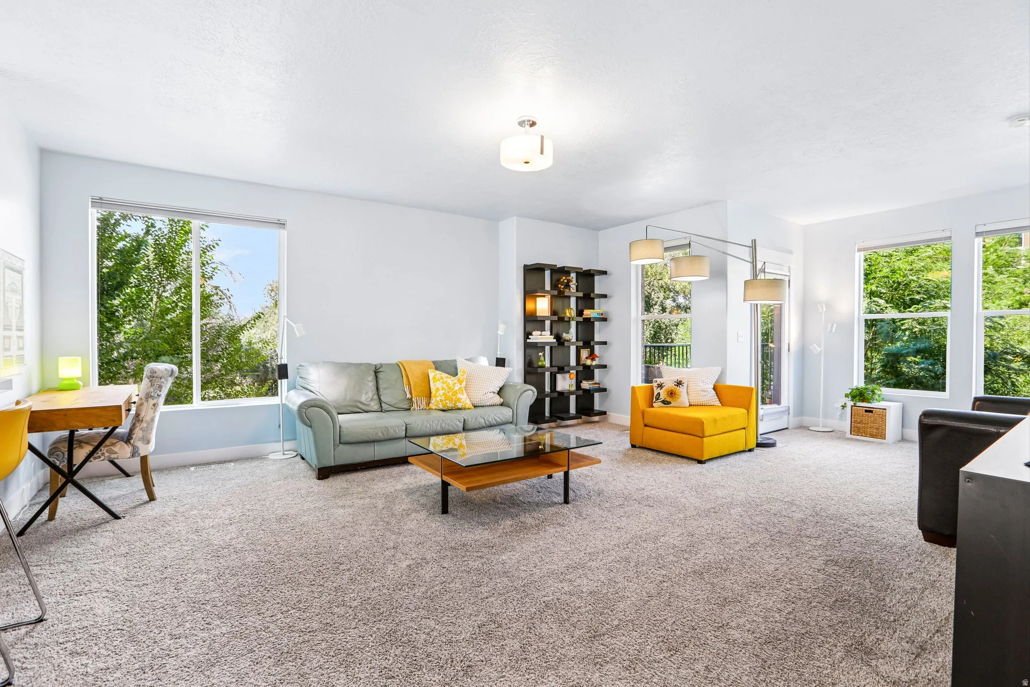 Expansive carpeting, multiple large windows, a built-in bookshelf, and a glass-top coffee table