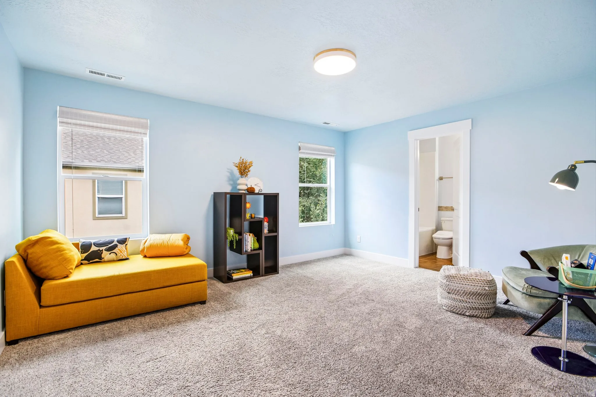 Bright, light-filled bedroom with soft blue walls, recessed ceiling lighting, and neutral carpet flooring