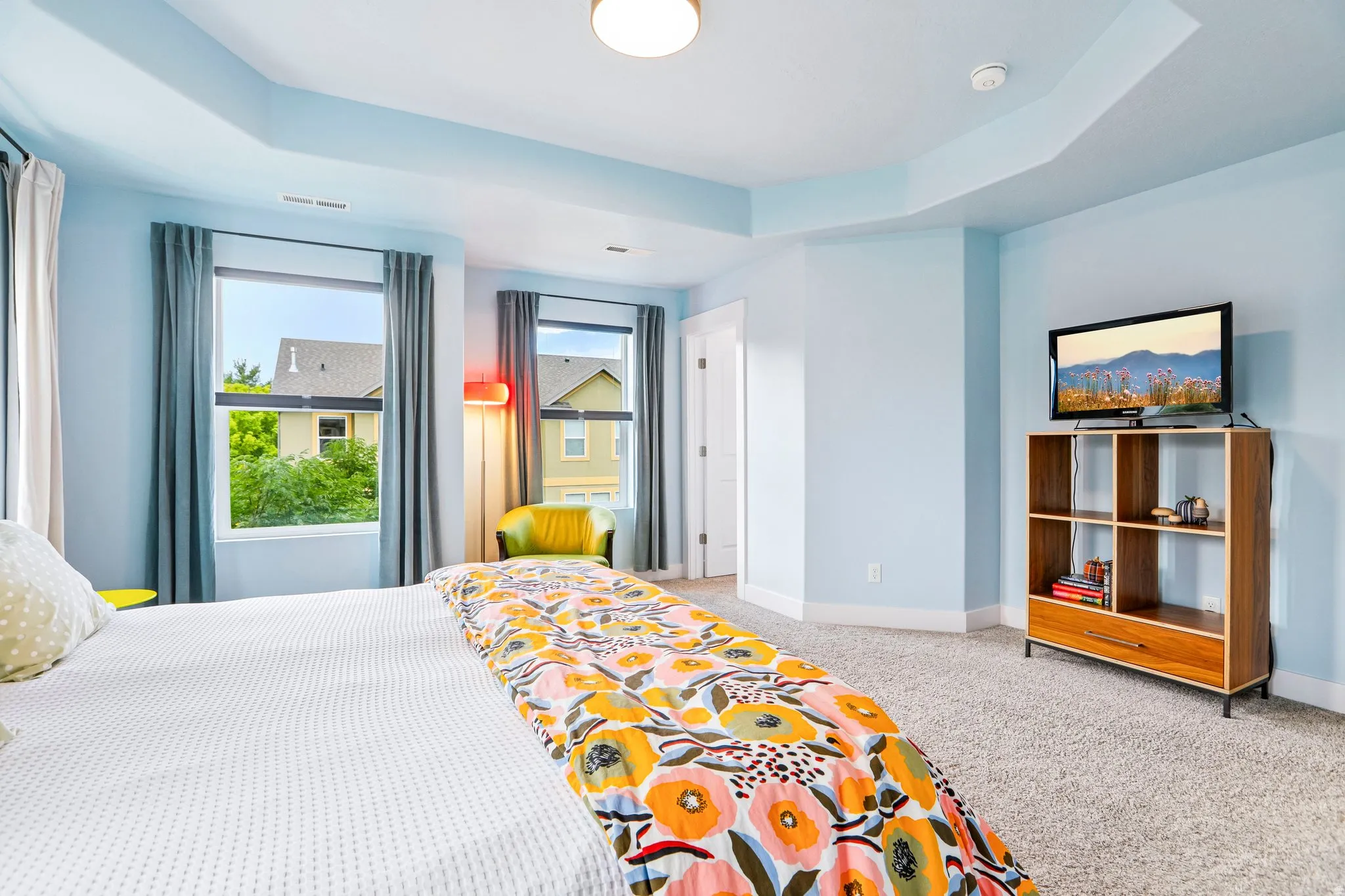 Tray ceiling with recessed lighting, multiple windows with neutral drapes, and light-toned carpeting