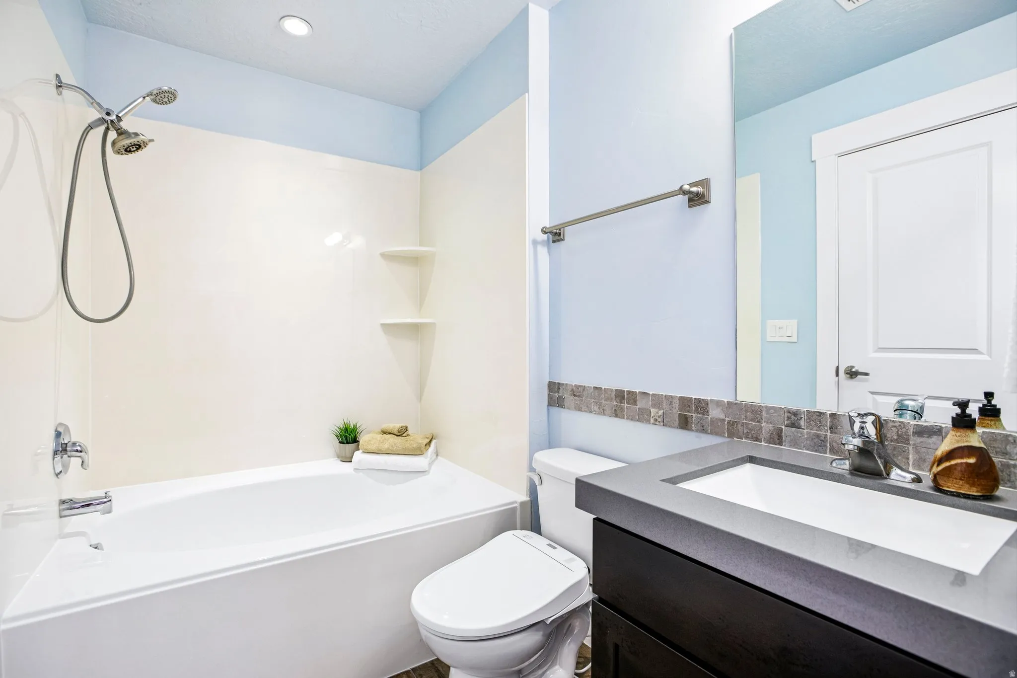 Full bathroom featuring a tub/shower combination, dark wood-finish vanity with an integrated sink, and an accent tile backsplash
