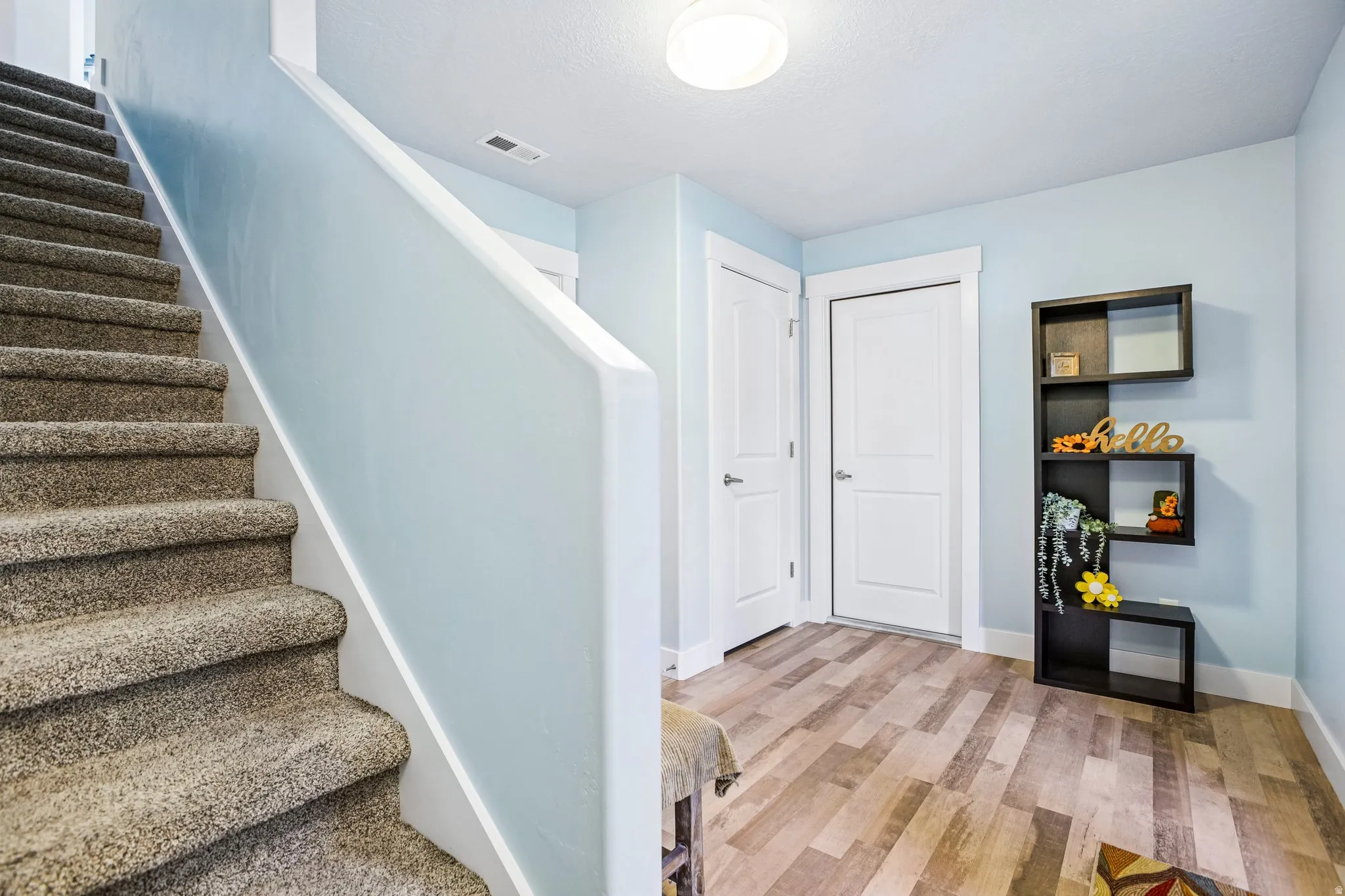Welcoming entryway featuring a curved staircase with carpeted treads and white railings, wood-finish flooring, recessed ceiling lighting, and built-in wall shelving with display space