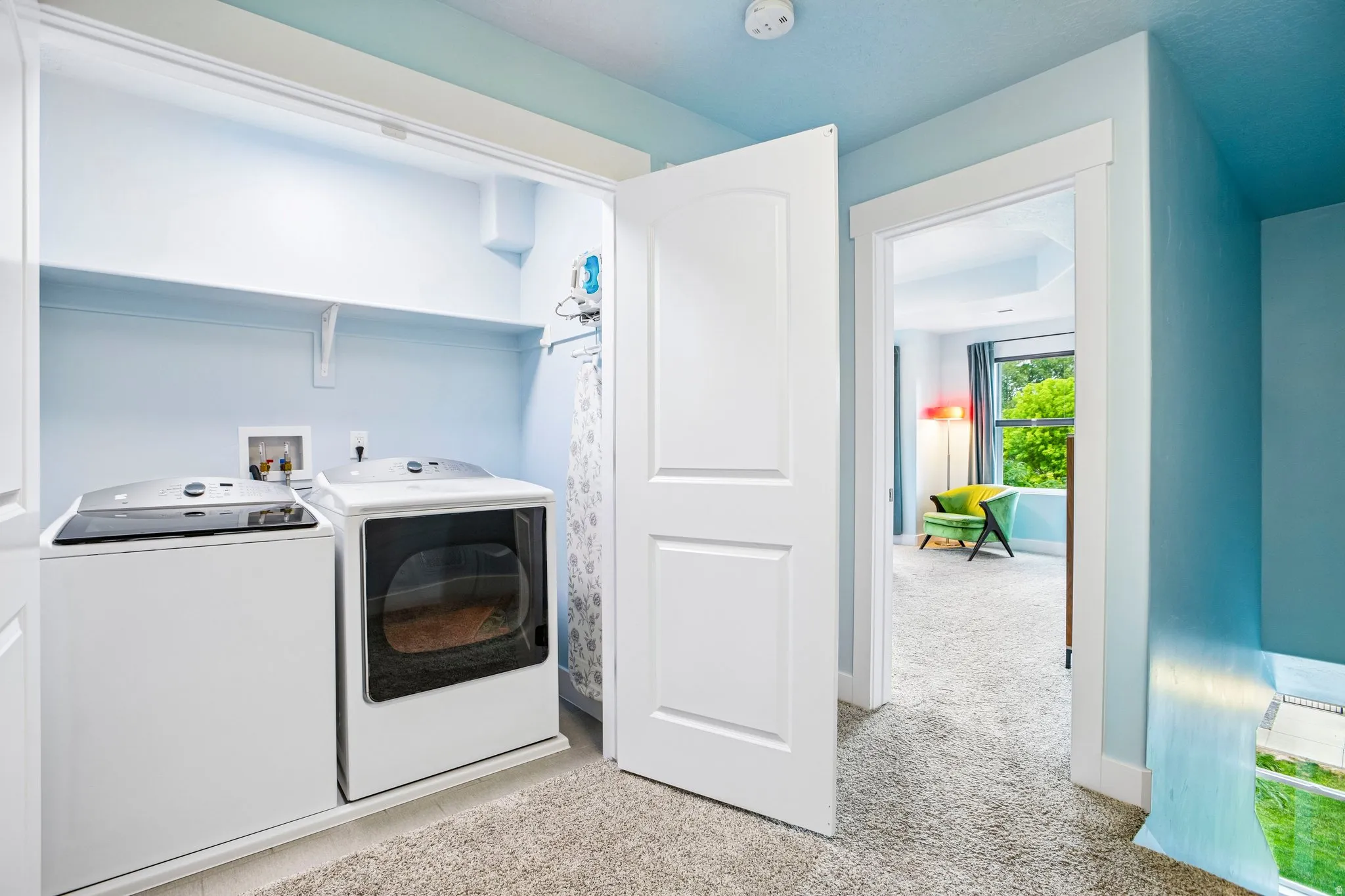 Dedicated laundry room featuring front-load washer and electric dryer with white cabinetry, carpeted flooring, and abundant natural light from overhead fixtures
