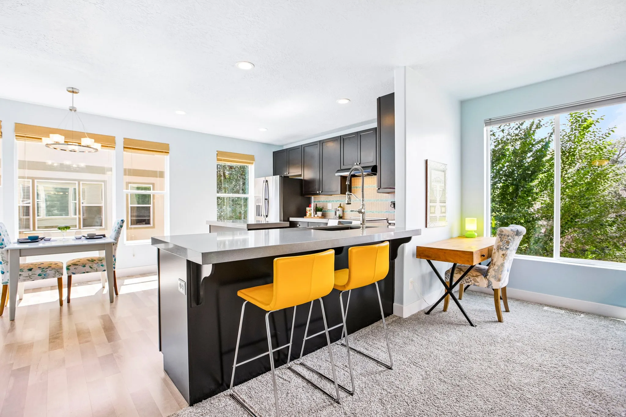 Kitchen island with a light-toned countertop and dark cabinetry, wood-finish flooring, recessed lighting, and a dining area with a contemporary chandelier
