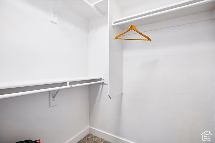 Spacious walk-in closet featuring white painted walls, polished concrete flooring, a sturdy metal hanging rod, and wooden hanger—ideal for organized storage and wardrobe display