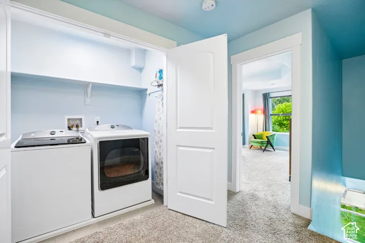 Dedicated laundry room featuring front-load washer and electric dryer with white cabinetry, carpeted flooring, and abundant natural light from overhead fixtures