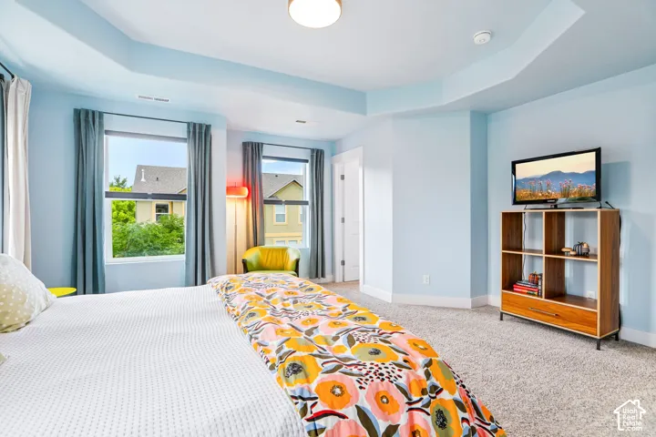 Tray ceiling with recessed lighting, multiple windows with neutral drapes, and light-toned carpeting