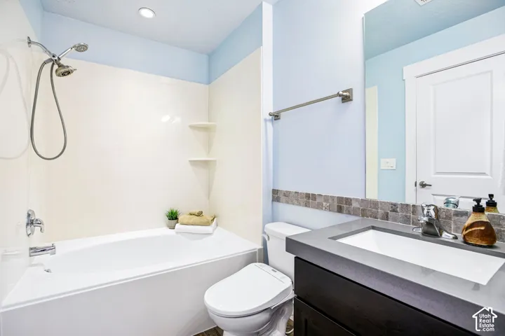 Full bathroom featuring a tub/shower combination, dark wood-finish vanity with an integrated sink, and an accent tile backsplash