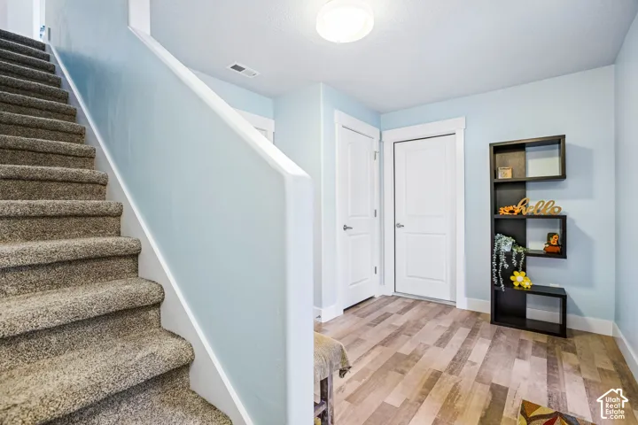 Welcoming entryway featuring a curved staircase with carpeted treads and white railings, wood-finish flooring, recessed ceiling lighting, and built-in wall shelving with display space