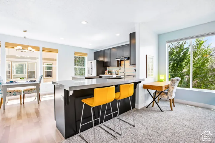 Kitchen island with a light-toned countertop and dark cabinetry, wood-finish flooring, recessed lighting, and a dining area with a contemporary chandelier