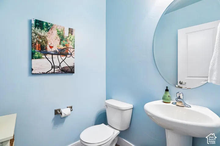 Bright, light-filled powder room featuring soft blue walls, a pedestal sink with single-handle faucet, a low-profile toilet, and a large round mirror