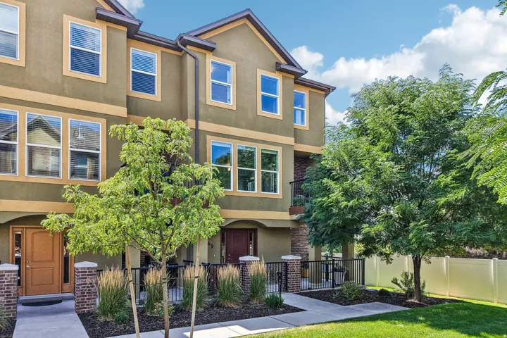 Three-story townhouse with a stucco exterior, multiple windows, a wrought iron balcony, and a walkway leading to the front entry