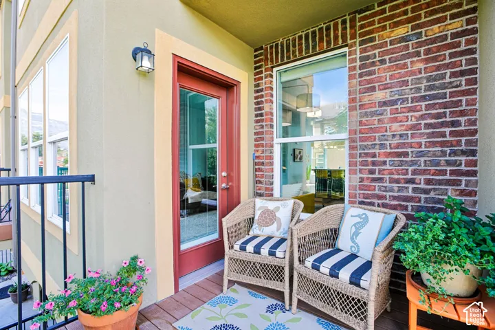 Exterior balcony featuring a wood-finish deck, brick accent wall, and a full-light entry door
