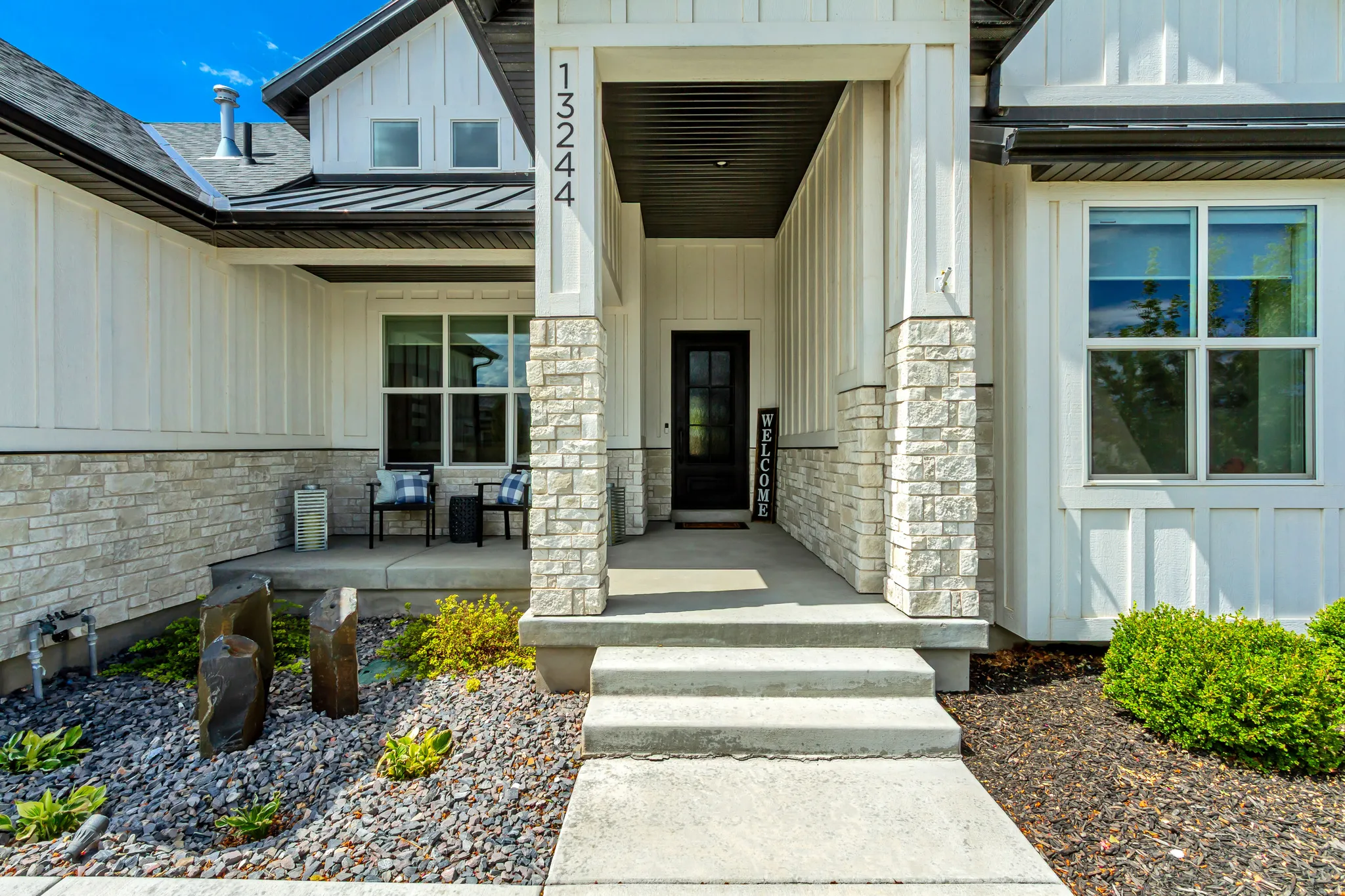 Board and batten siding with stone accents, covered front entry, dark-framed windows, and concrete walkway