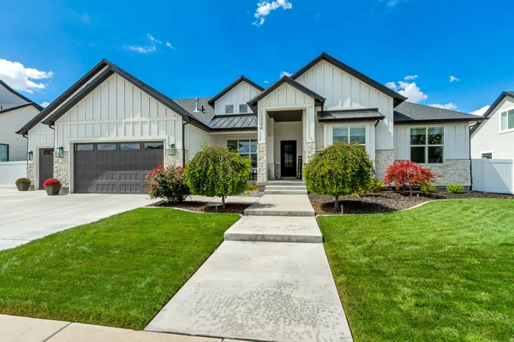 Two-car garage, manicured lawn, concrete walkway, stone veneer facade, and crisp white board and batten siding