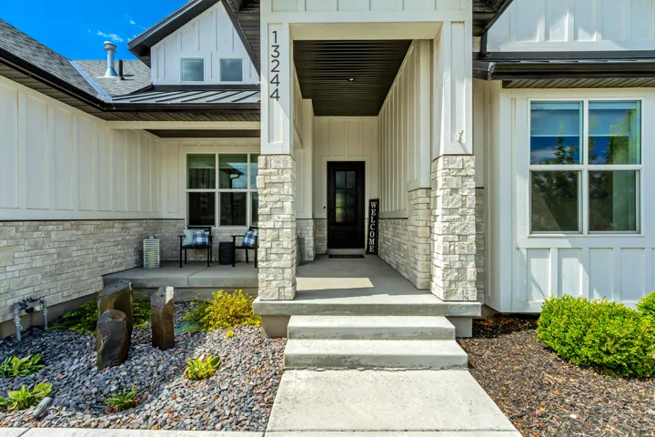 Board and batten siding with stone accents, covered front entry, dark-framed windows, and concrete walkway