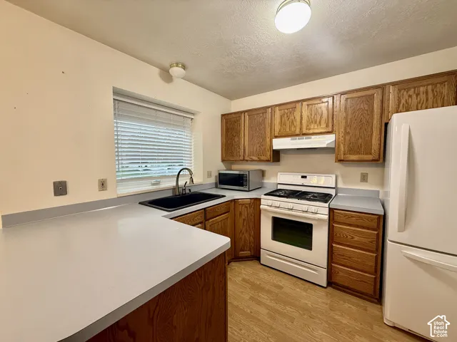 Kitchen featuring wood-finish flooring, wood cabinetry, light-toned countertops, and a black composite sink with a gooseneck faucet