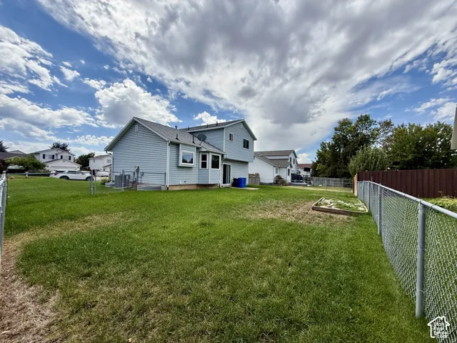 Expansive backyard featuring a chain-link fence, a raised garden bed, and a two-story residence with light blue siding
