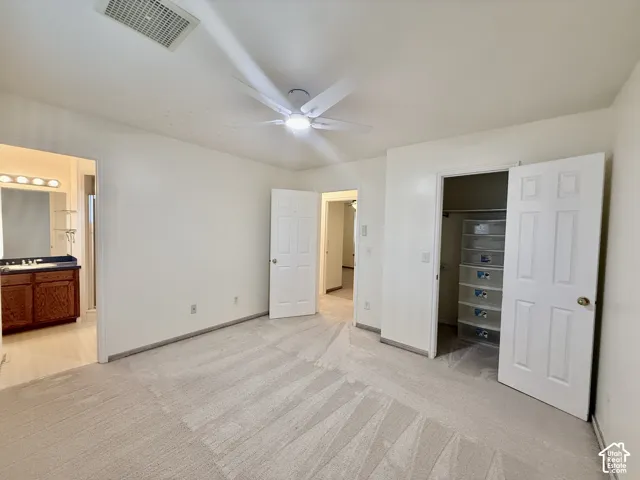 Ceiling fan with integrated lighting, carpeted flooring, built-in closet shelving, and a vanity with a wood-finish cabinet and countertop