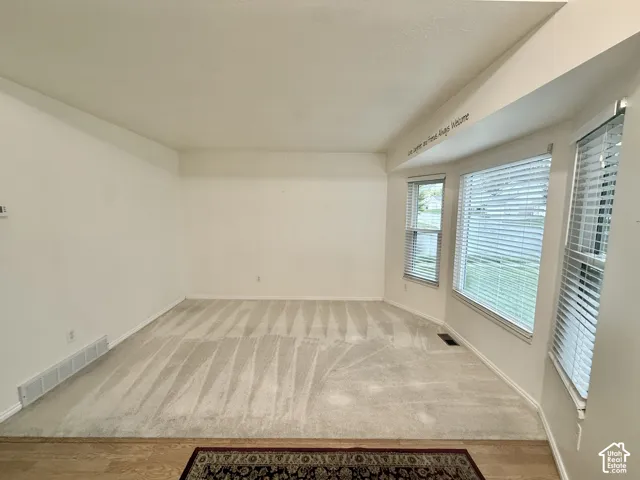 Bright, light-filled room showcasing pristine wood-finish flooring, expansive windows with plantation shutters providing natural illumination, and clean white walls and ceiling