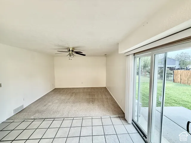 Expansive carpeted area with a ceiling fan, illuminated by natural light from the sliding glass doors, leading to an outdoor patio and green space