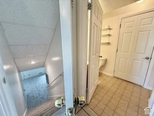 Tiled flooring entry with a paneled door, leading to a half-bath with wall-mounted shelving and a toilet