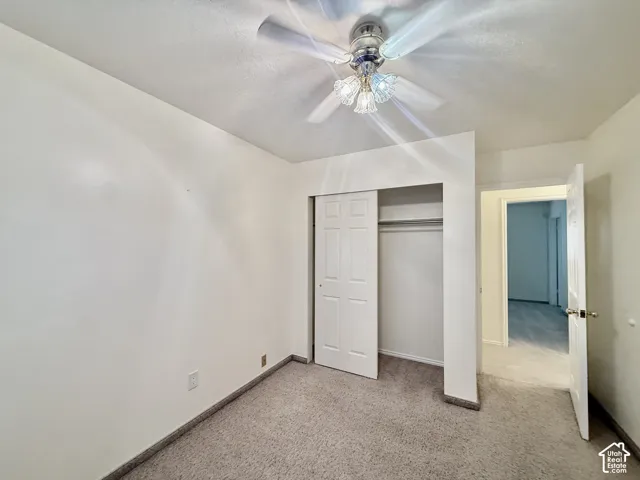 Textured wall finishes, carpeted flooring, ceiling fan with integrated lighting, and a closet with bi-fold doors