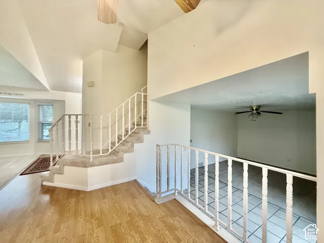 Wood-finish flooring, carpeted staircase with white railings, textured tile flooring, recessed window, and ceiling fan