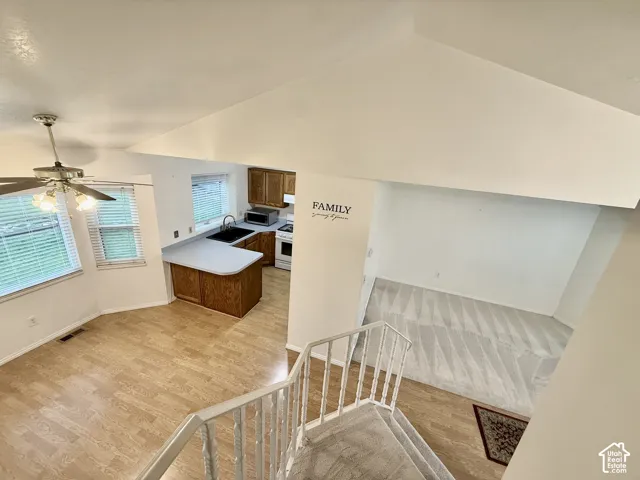 Vaulted ceiling, wood-finish flooring, wood cabinetry, light-toned countertops, and a ceiling fan with integrated lighting
