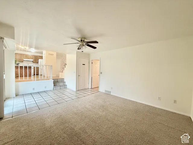 Carpeted living area with tile flooring transition, ceiling fan, and staircase