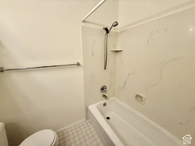 Built-in tub with a shower panel featuring a handheld showerhead and an integrated corner shelf