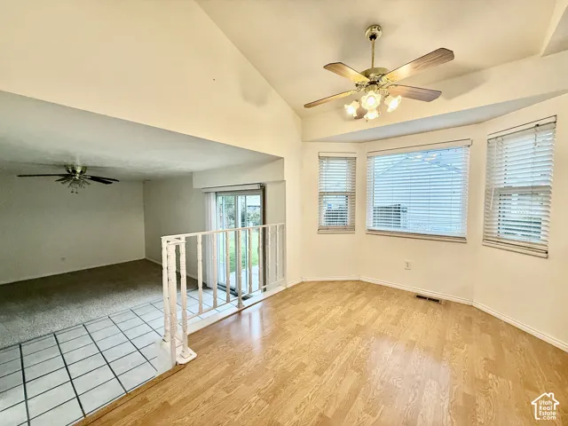 Vaulted ceiling with a ceiling fan, bay window with blinds, wood-finish flooring, and a tiled entry