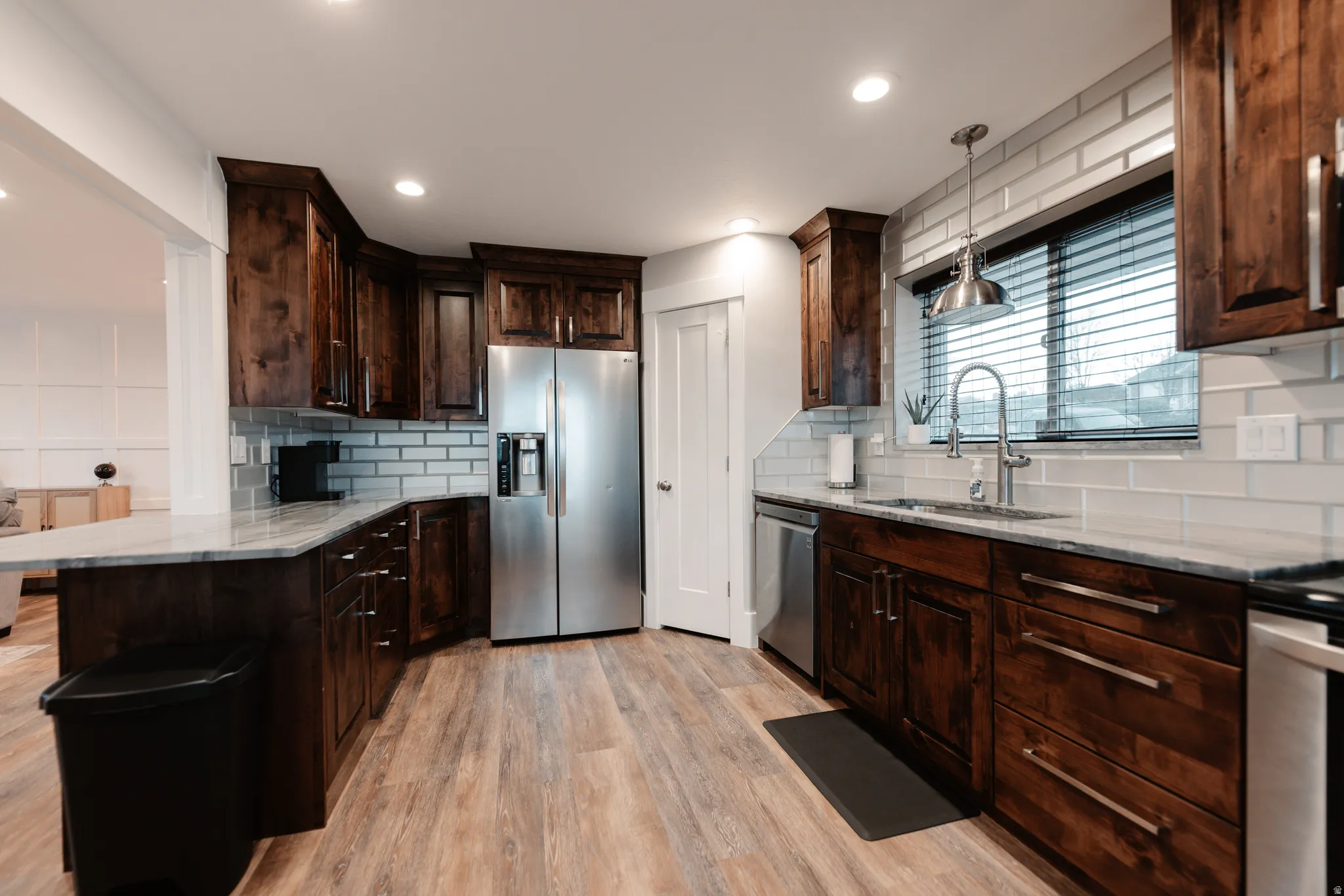 Modern kitchen showcasing rich wood cabinetry, stainless steel appliances including a side-by-side refrigerator, subway tile backsplash, and quartz countertops