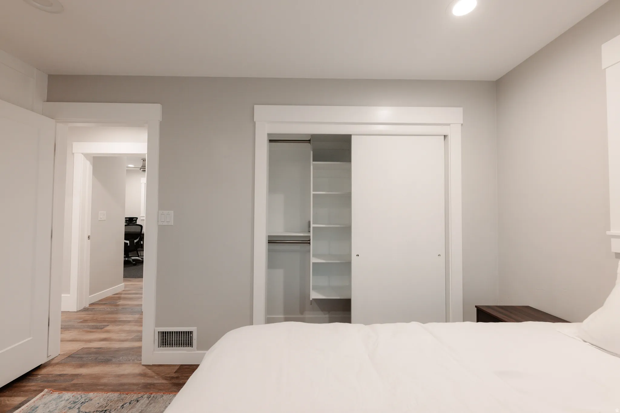 Bright primary bedroom featuring recessed ceiling lighting, wood-finish flooring, and direct access to a spacious walk-in closet with built-in shelving and dual sliding doors