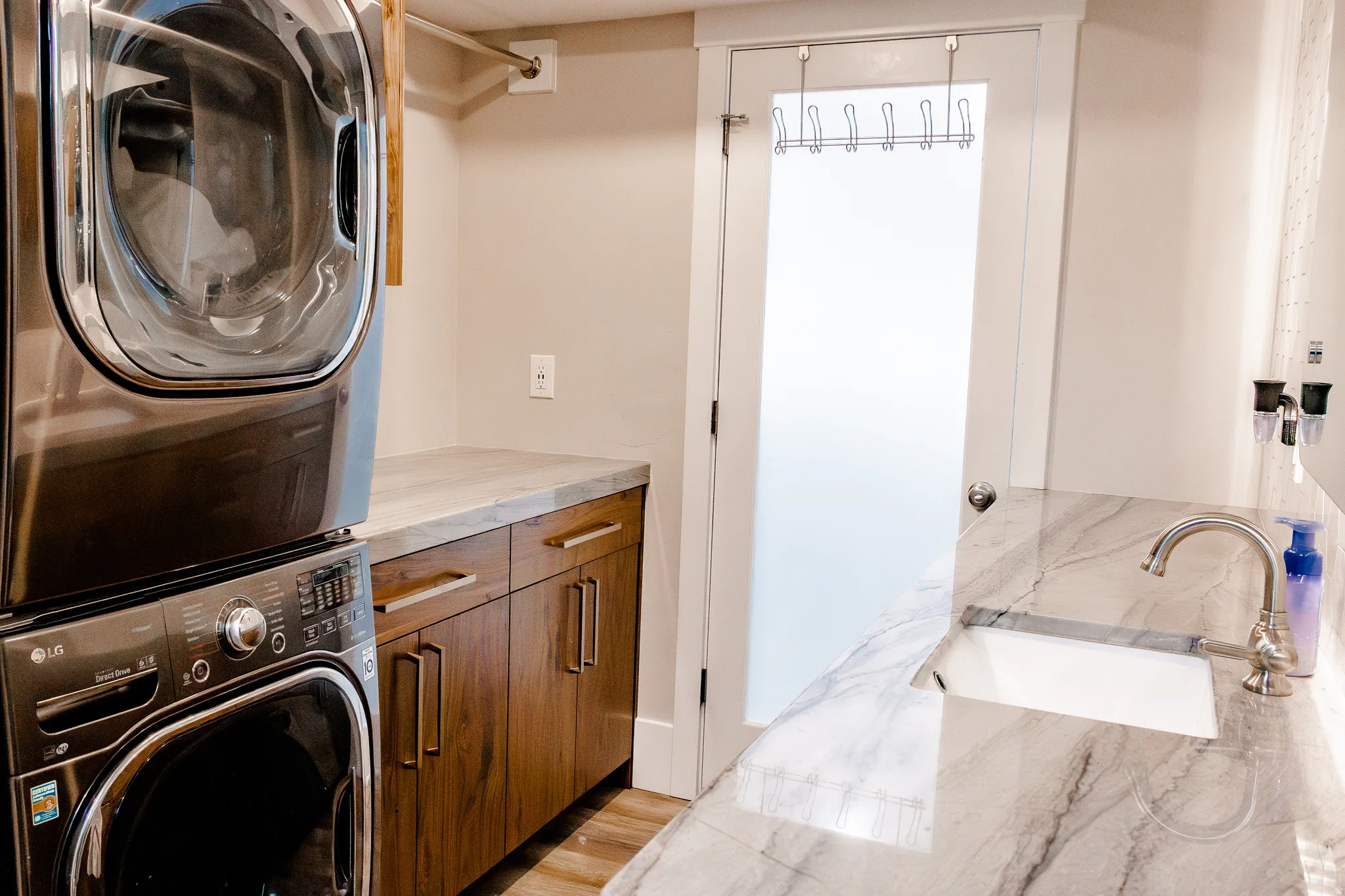Integrated laundry appliances with wood-finish cabinetry, a laundry sink, and a stone-finish countertop in basement