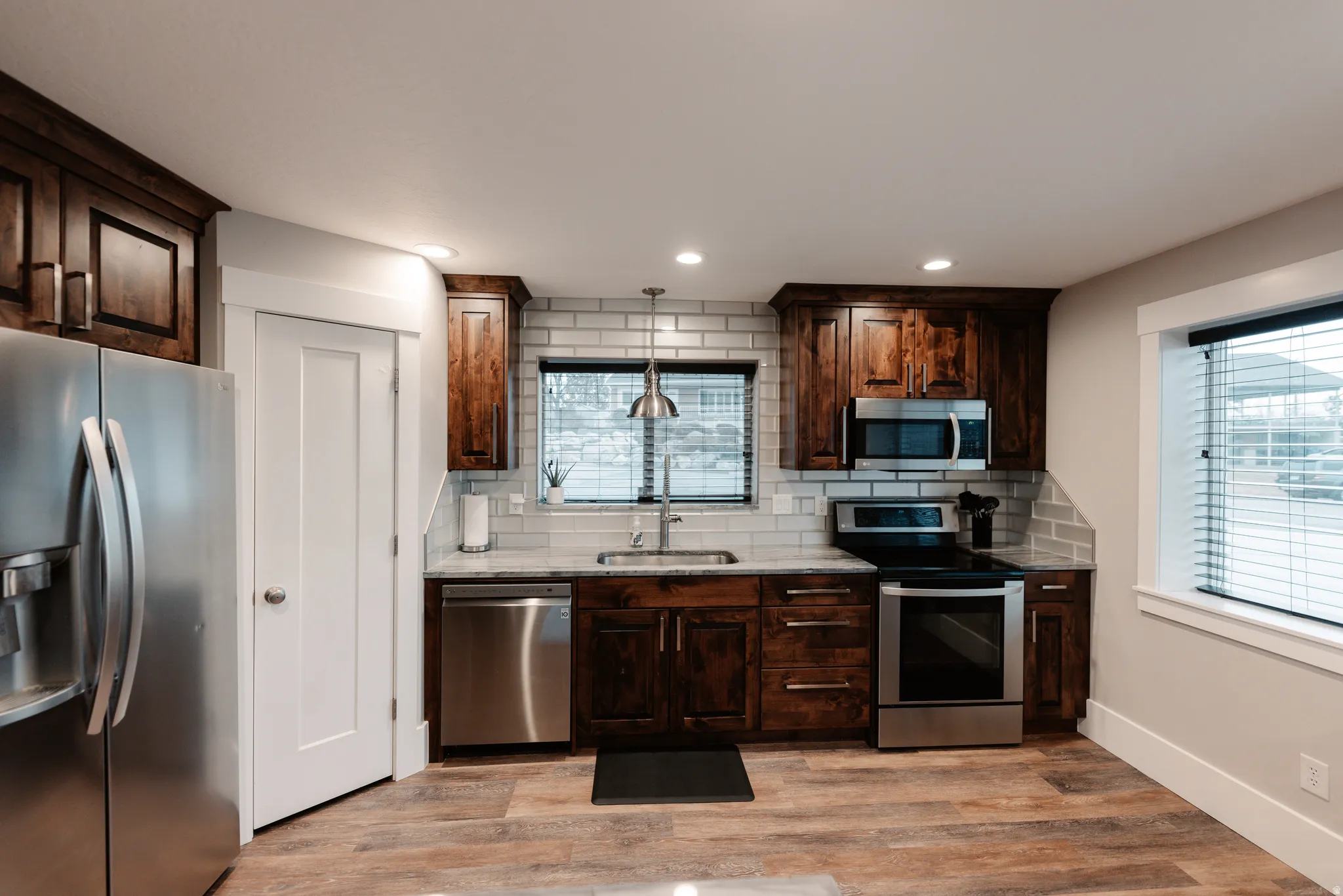 Updated kitchen featuring dark wood cabinetry, stainless steel appliances including a French-door refrigerator and electric range, subway tile backsplash, and wood-finish flooring throughout the space