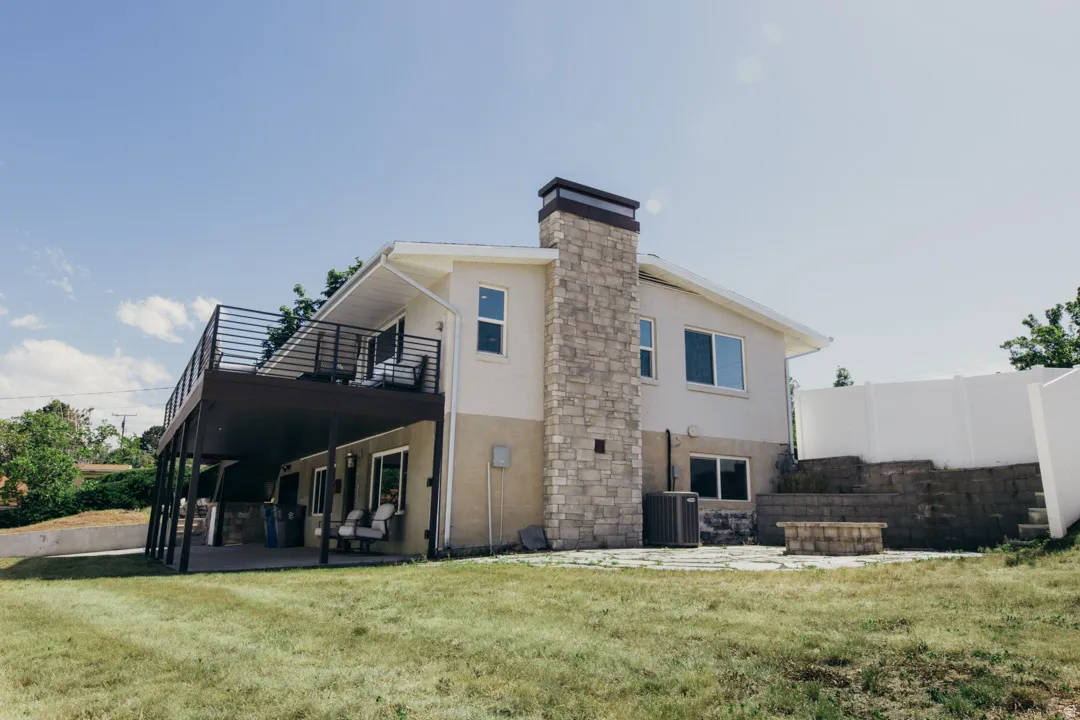 Modern two-story residence featuring a stone and stucco exterior, metal deck railing, multi-pane windows, and a chimney