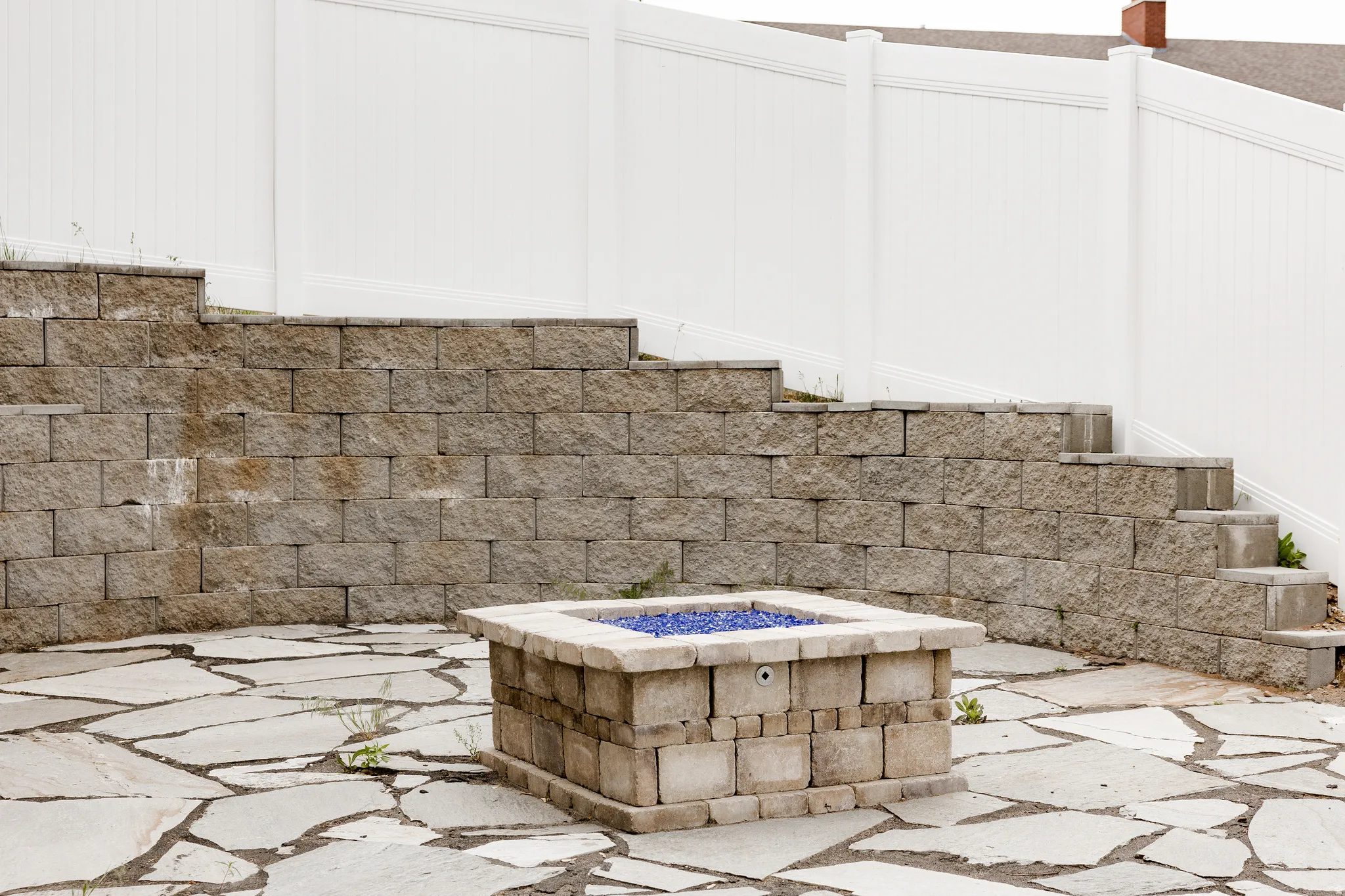 Outdoor entertaining space featuring a custom stone fire pit with blue  accents, set atop a flagstone patio